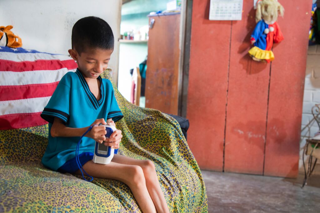 Levi sits on his bed with his medical device that helps him administer growth hormones